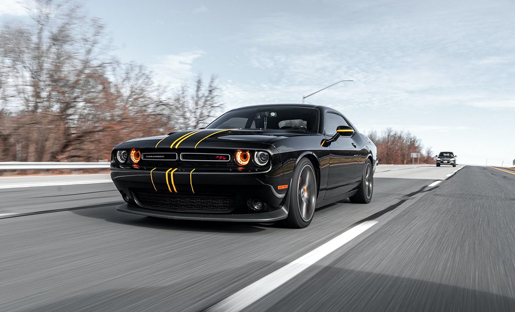 A black car with yellow stripes driving down the road.